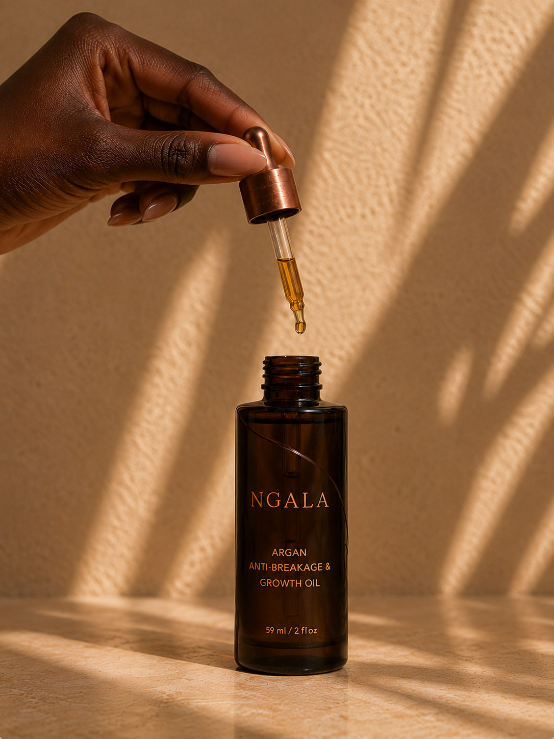 A dropper of Argan Anti-Breakage & Growth Oil held over warm stone